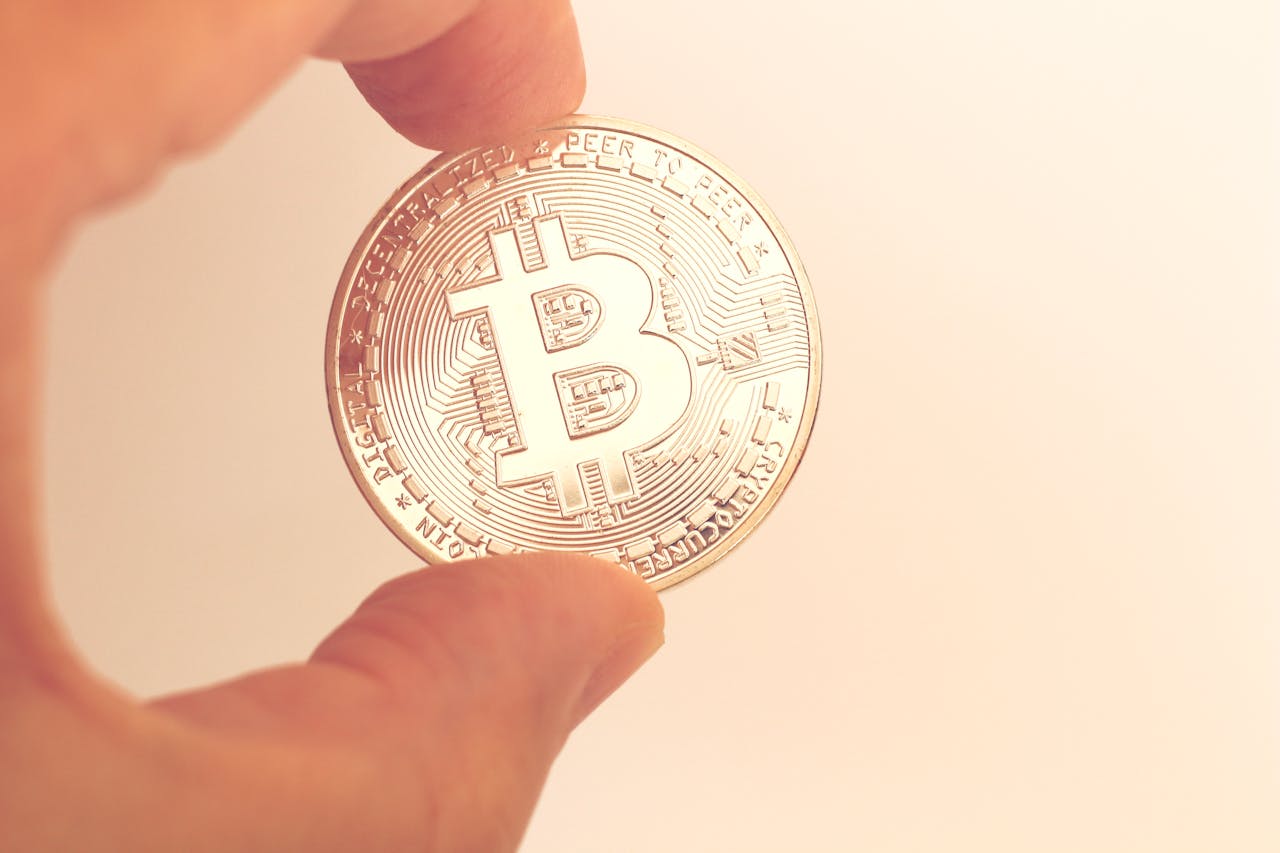 A close-up image of a hand holding a Bitcoin coin against a neutral background.